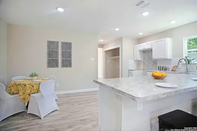 kitchen with sink, light stone counters, backsplash, light hardwood / wood-style floors, and white cabinets