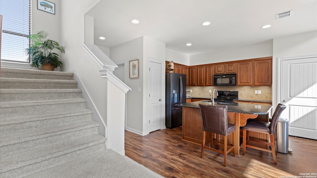 kitchen featuring decorative backsplash, a breakfast bar area, a center island with sink, black appliances, and dark hardwood / wood-style flooring