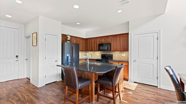 kitchen featuring decorative backsplash, dark hardwood / wood-style flooring, a kitchen island with sink, black appliances, and sink