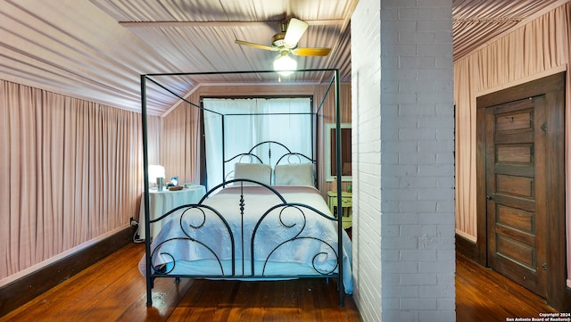 bedroom featuring dark wood-type flooring, brick wall, and lofted ceiling