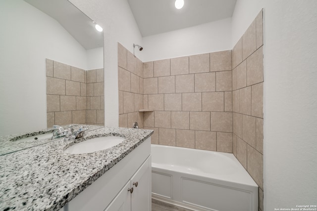 bathroom featuring tiled shower / bath, vanity, and vaulted ceiling