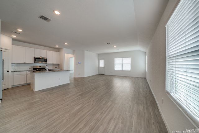 kitchen featuring stone countertops, a kitchen island with sink, white cabinetry, appliances with stainless steel finishes, and light hardwood / wood-style floors