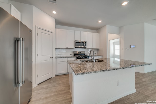 kitchen with appliances with stainless steel finishes, sink, light hardwood / wood-style floors, white cabinets, and a center island with sink