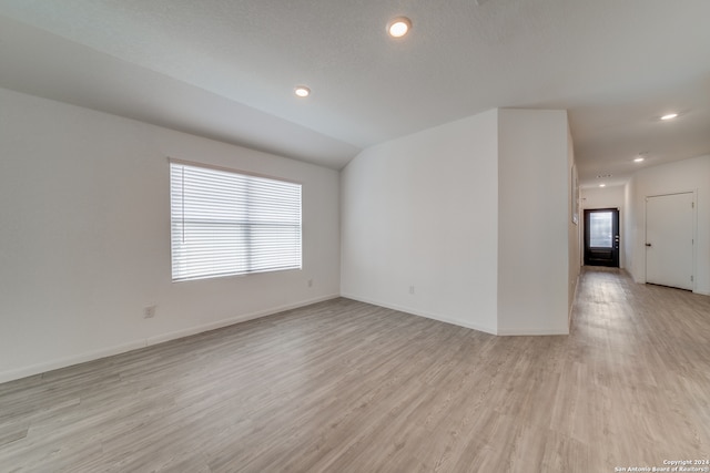 empty room with vaulted ceiling, a textured ceiling, and light wood-type flooring