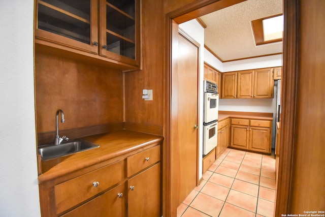 kitchen with double oven, crown molding, sink, a textured ceiling, and stainless steel refrigerator