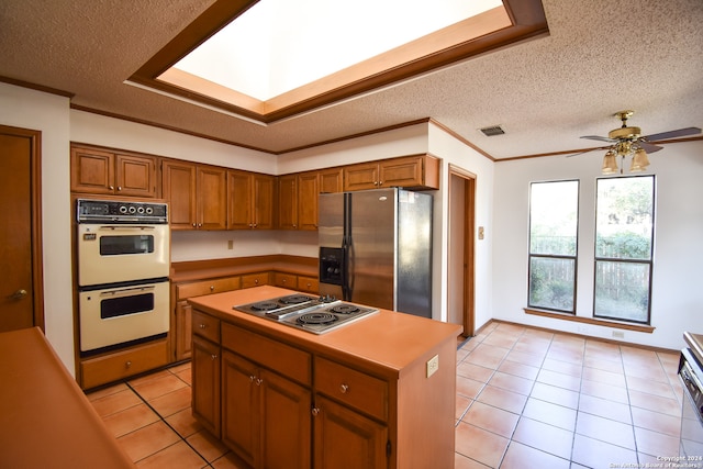 kitchen with a kitchen island, a textured ceiling, ceiling fan, stainless steel appliances, and light tile patterned floors