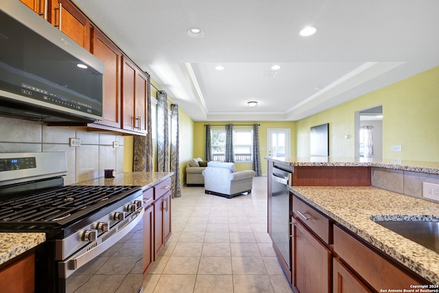 kitchen featuring appliances with stainless steel finishes, a raised ceiling, light stone counters, decorative backsplash, and light tile patterned floors