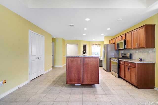 kitchen with light tile patterned flooring, an island with sink, stainless steel appliances, light stone counters, and decorative backsplash