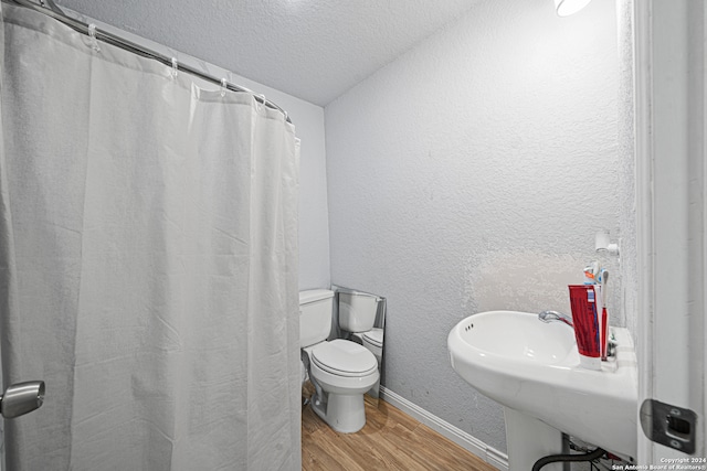 bathroom with a textured ceiling, hardwood / wood-style flooring, walk in shower, vaulted ceiling, and toilet