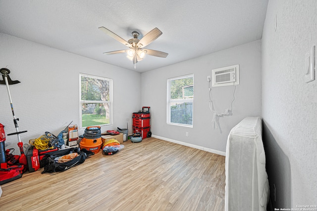 playroom featuring a wall mounted AC, light hardwood / wood-style flooring, a textured ceiling, and ceiling fan