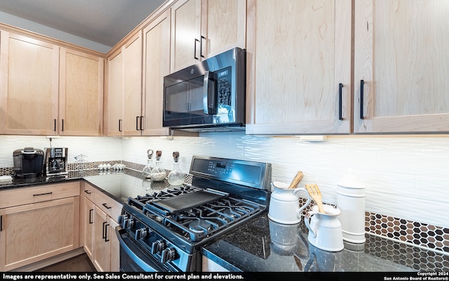 kitchen with gas stove, light brown cabinetry, and dark stone counters