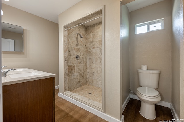 bathroom with toilet, hardwood / wood-style flooring, vanity, and tiled shower