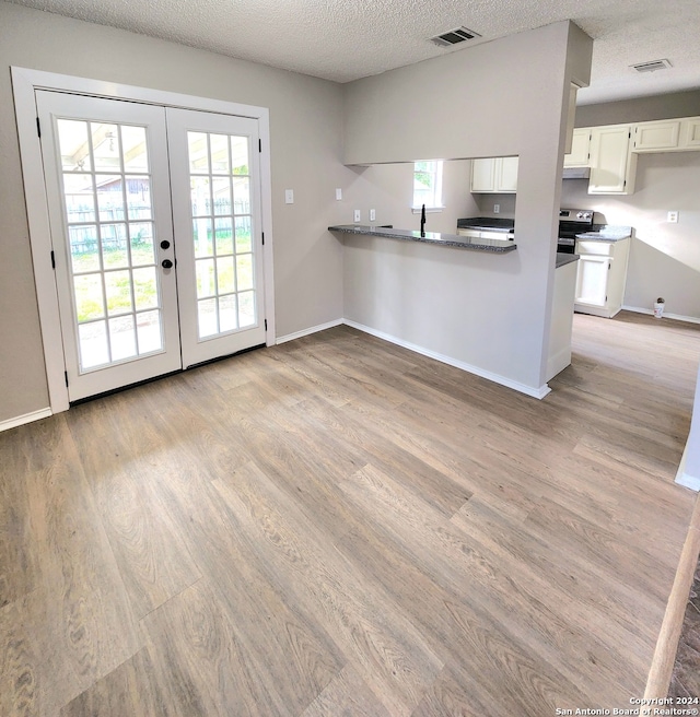 kitchen with french doors, white cabinetry, light wood-type flooring, and kitchen peninsula