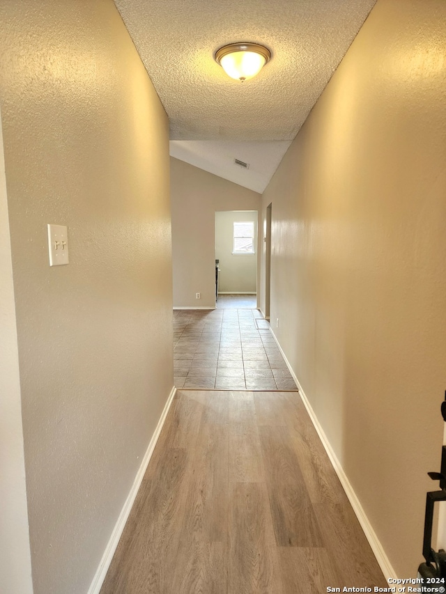 hall with a textured ceiling, wood-type flooring, and lofted ceiling