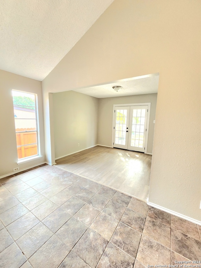 unfurnished room with lofted ceiling, french doors, a healthy amount of sunlight, and a textured ceiling