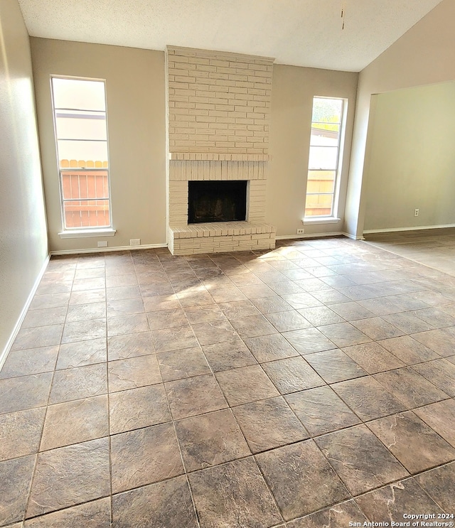 unfurnished living room with vaulted ceiling, a brick fireplace, and a textured ceiling