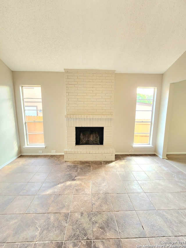 unfurnished living room featuring a textured ceiling and a brick fireplace