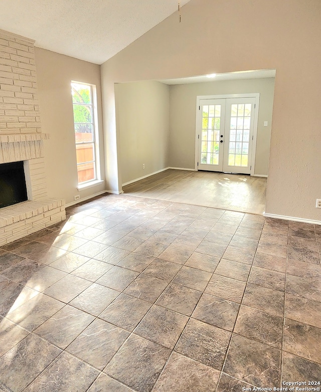 unfurnished living room featuring french doors, vaulted ceiling, a fireplace, and a textured ceiling