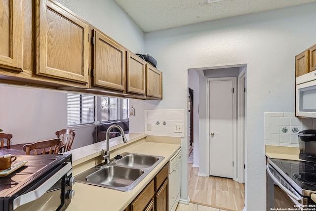 kitchen with white appliances, sink, backsplash, a textured ceiling, and light hardwood / wood-style flooring