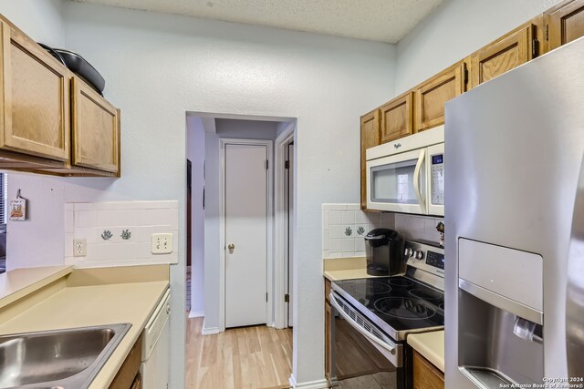 kitchen featuring decorative backsplash, appliances with stainless steel finishes, a textured ceiling, light wood-type flooring, and sink