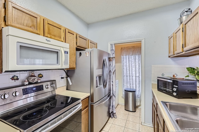 kitchen with appliances with stainless steel finishes, decorative backsplash, light tile patterned flooring, and sink