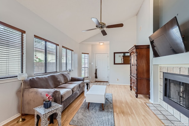 living room with high vaulted ceiling, a tiled fireplace, light hardwood / wood-style floors, and ceiling fan