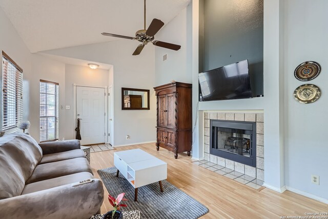 living room with light hardwood / wood-style flooring, a tiled fireplace, high vaulted ceiling, and ceiling fan