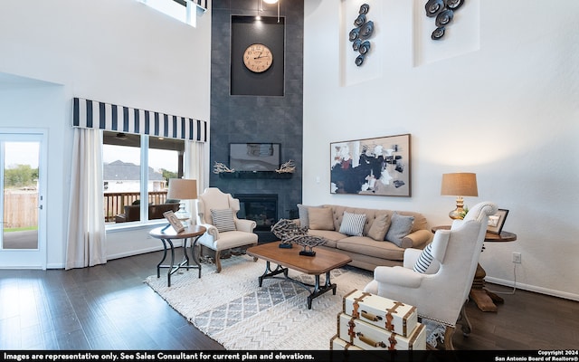 living room with dark wood-type flooring, a towering ceiling, plenty of natural light, and a tile fireplace