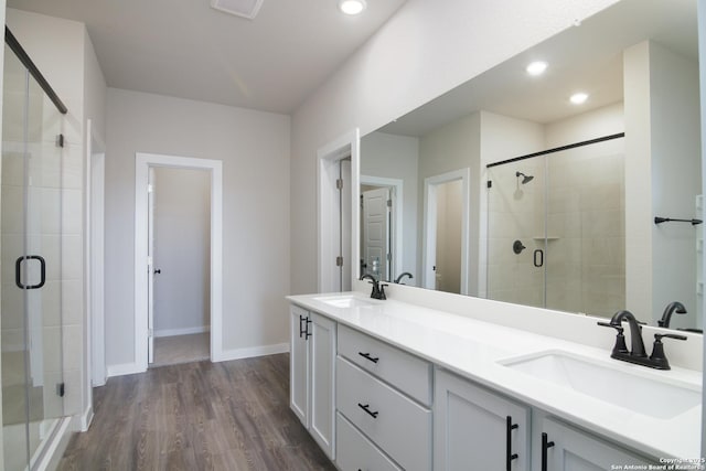 bathroom featuring double vanity, a sink, a shower stall, and wood finished floors