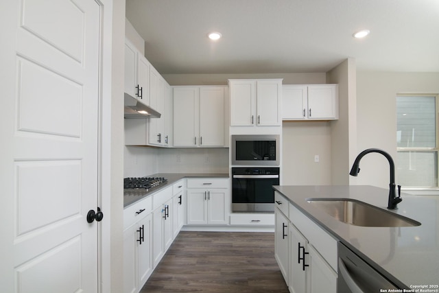 kitchen with dark countertops, stainless steel gas cooktop, under cabinet range hood, white cabinetry, and a sink