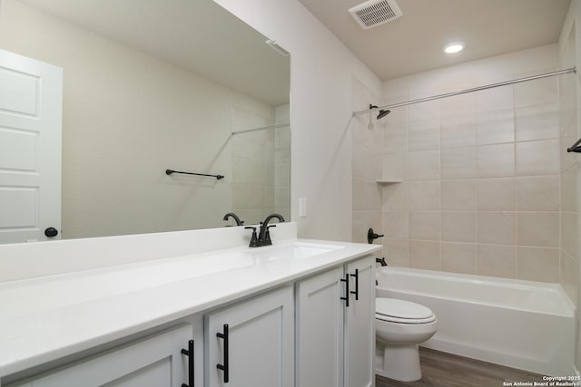 bathroom featuring visible vents, toilet, vanity, shower / tub combination, and wood finished floors