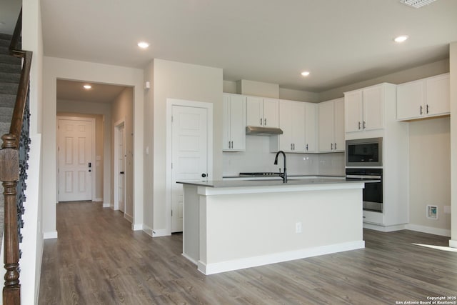 kitchen featuring a kitchen island with sink, oven, built in microwave, and white cabinetry