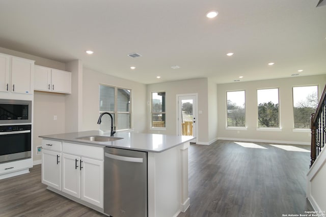 kitchen with an island with sink, open floor plan, stainless steel appliances, white cabinetry, and a sink