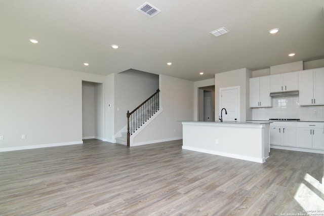 kitchen with open floor plan, a kitchen island with sink, visible vents, and white cabinetry