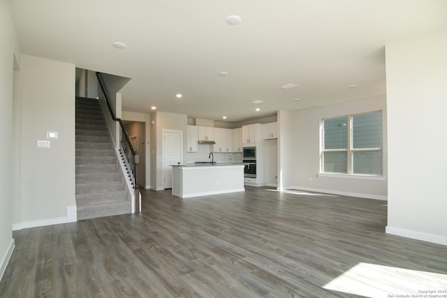 unfurnished living room with dark wood-type flooring, recessed lighting, stairway, and baseboards