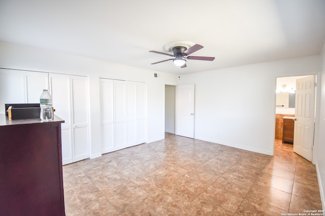 unfurnished bedroom featuring multiple closets, light tile patterned flooring, ensuite bathroom, and ceiling fan