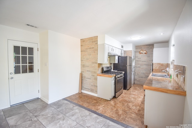 kitchen with sink, white cabinets, light tile patterned floors, tile walls, and appliances with stainless steel finishes