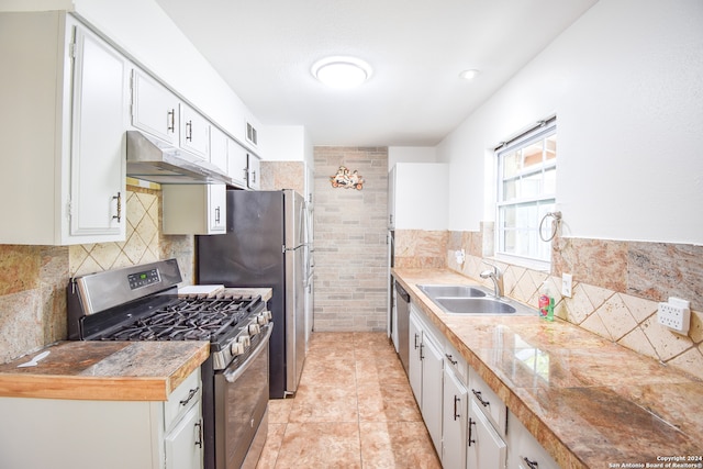 kitchen with white cabinetry, tile walls, light tile patterned flooring, sink, and stainless steel gas range