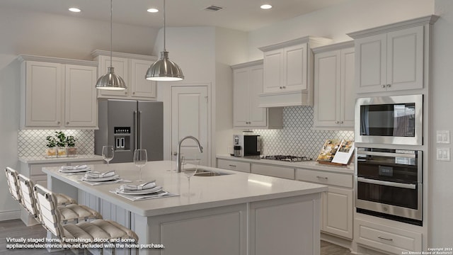 kitchen with hanging light fixtures, backsplash, a kitchen island with sink, sink, and stainless steel appliances