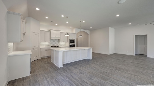 kitchen featuring a kitchen island with sink, backsplash, pendant lighting, light wood-type flooring, and white cabinetry