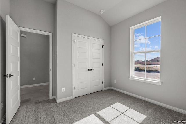 unfurnished bedroom featuring a closet, baseboards, carpet flooring, and lofted ceiling