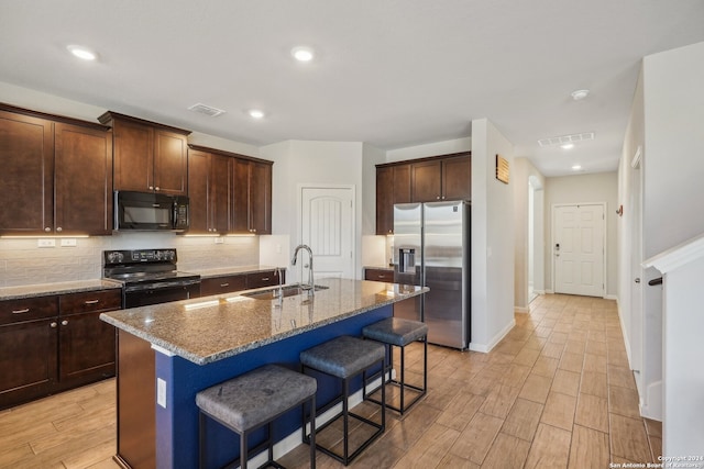 kitchen featuring black appliances, sink, an island with sink, dark stone countertops, and light hardwood / wood-style flooring