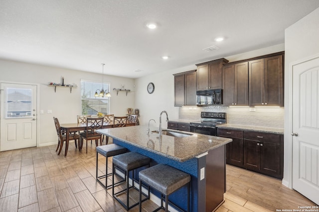 kitchen with black appliances, sink, light hardwood / wood-style floors, dark stone countertops, and a kitchen island with sink