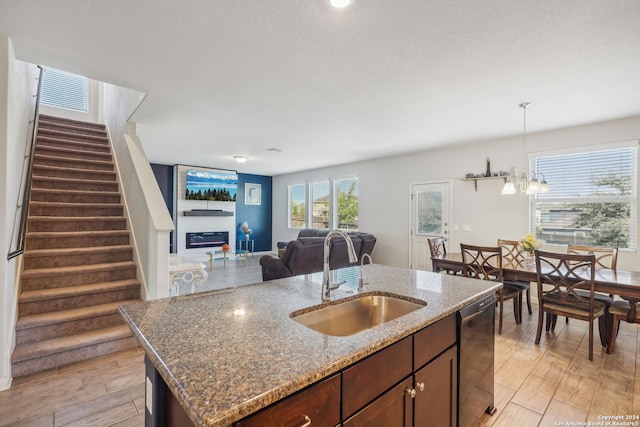 kitchen with sink, light wood-type flooring, stone countertops, a notable chandelier, and a kitchen island with sink