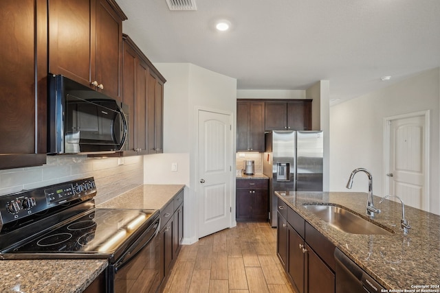 kitchen featuring light hardwood / wood-style flooring, backsplash, dark stone counters, sink, and black appliances