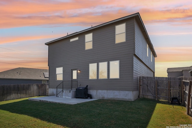 back house at dusk with a patio and a lawn