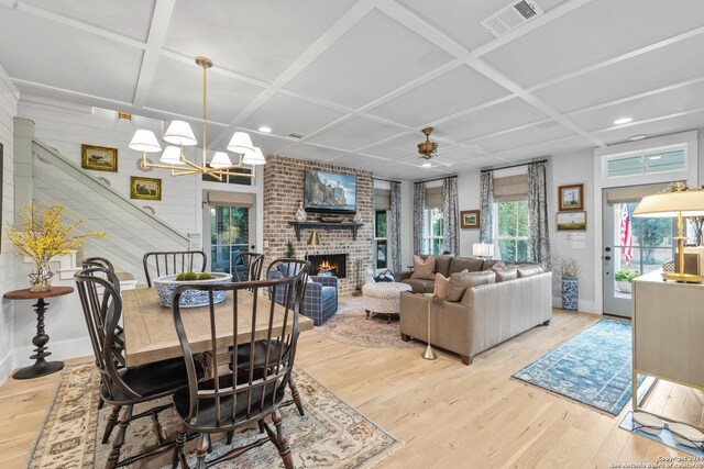 dining space featuring light hardwood / wood-style floors, coffered ceiling, ceiling fan with notable chandelier, and a brick fireplace