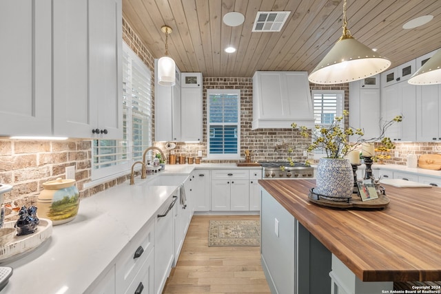 kitchen featuring white cabinets, a healthy amount of sunlight, pendant lighting, and wooden counters