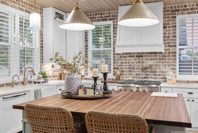 kitchen featuring wooden counters, dishwasher, brick wall, white cabinets, and stainless steel range oven