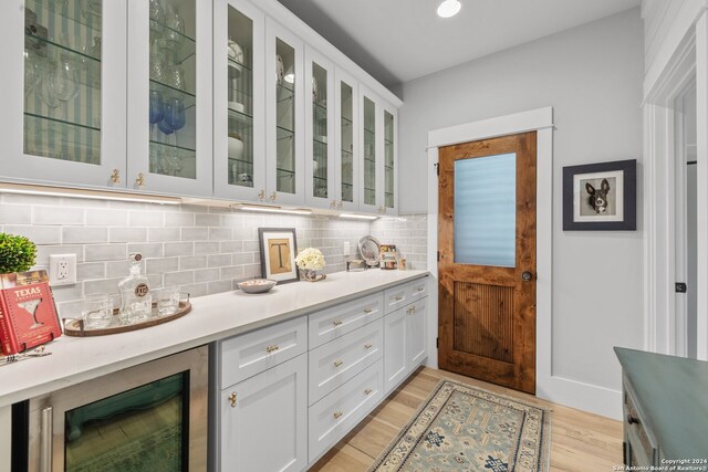 bar featuring light hardwood / wood-style floors, beverage cooler, decorative backsplash, and white cabinets